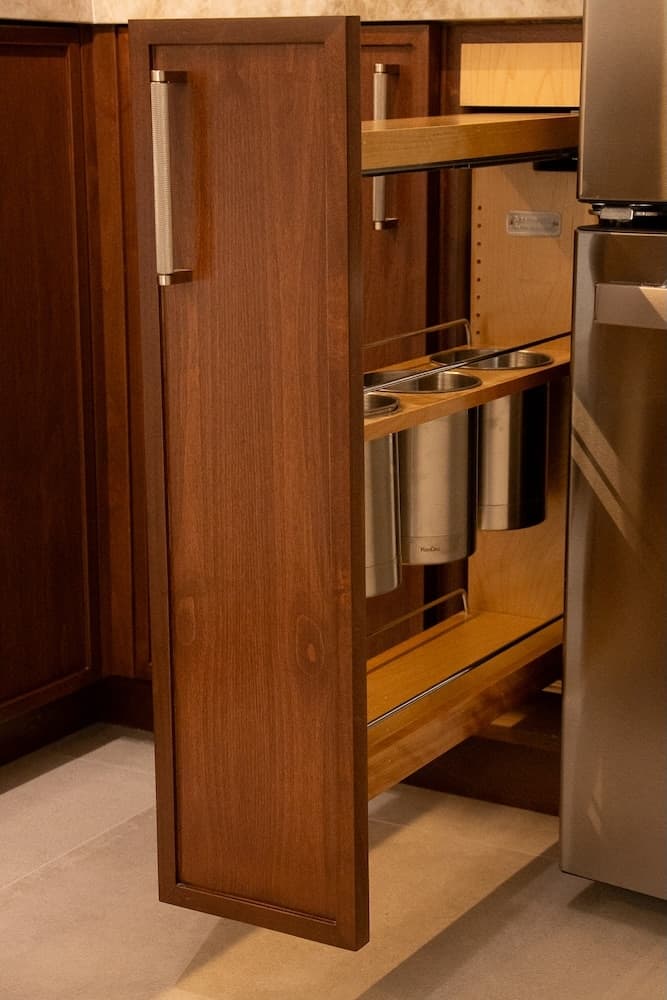 A wooden kitchen cabinet with a pull-out drawer holding stainless steel containers.