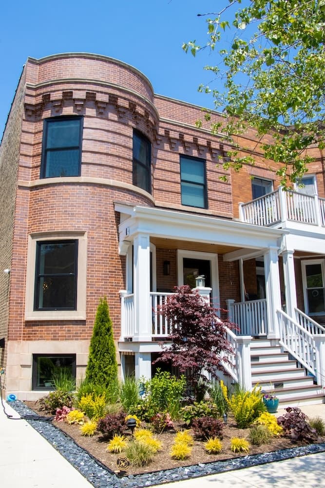 A brick house with a porch, decorated garden, and blue sky.