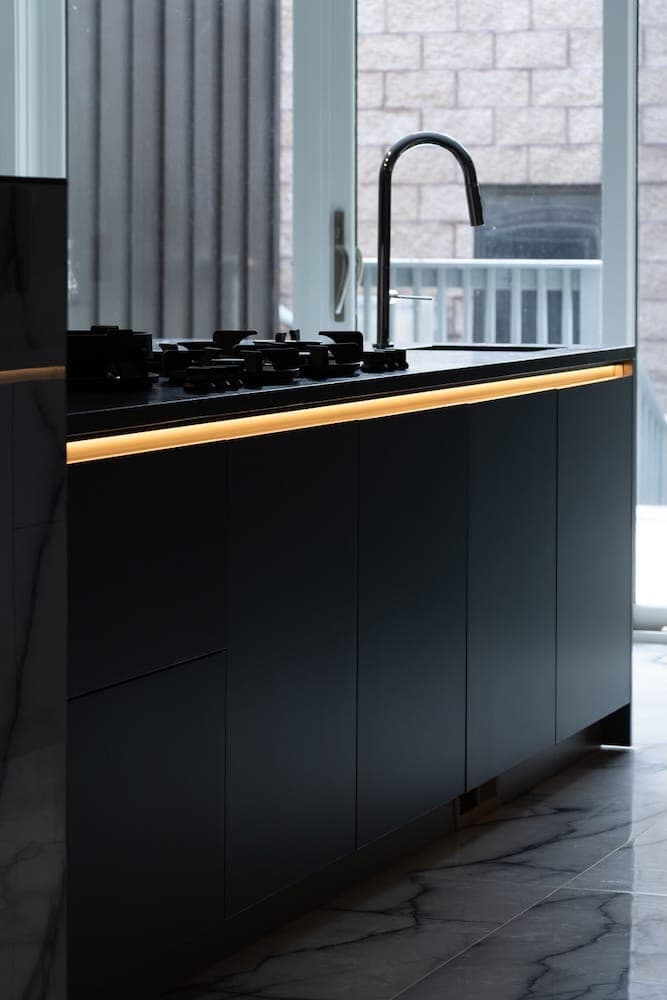 Black kitchen cabinets with lit edges beside a window