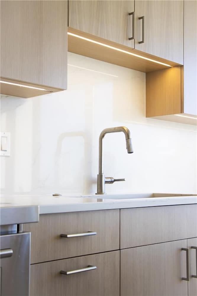 Modern kitchen with light wood cabinets a sleek sink and a marble backsplash